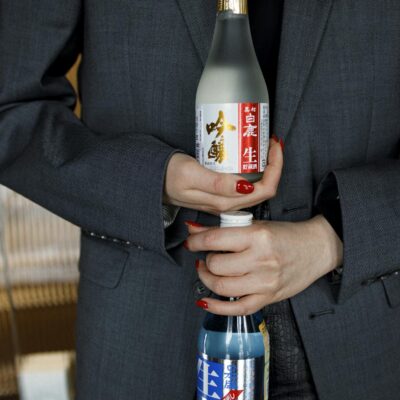 A woman in a suit holds two Japanese sake bottles, showcasing them with elegance.