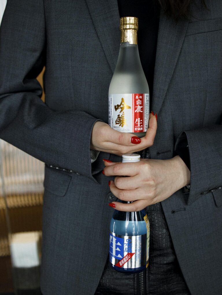 A woman in a suit holds two Japanese sake bottles, showcasing them with elegance.