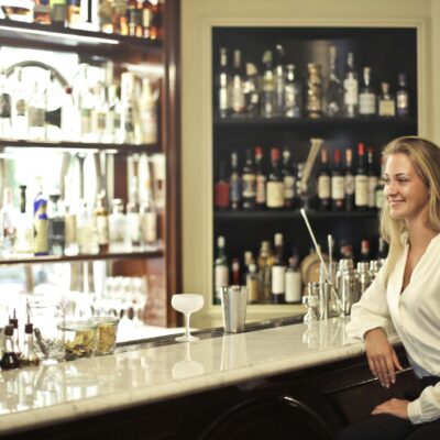 A woman sitting at a well-stocked bar with various alcoholic beverages, enjoying the ambiance.