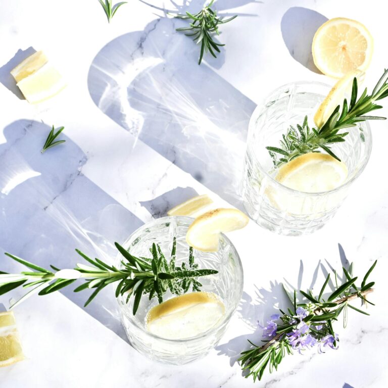 Bright and refreshing gin and tonic with lemon and rosemary on marble surface.