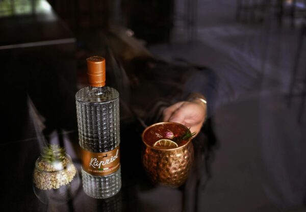 Close-up of a gin bottle and copper mug on glass table, perfect for cocktail enthusiasts.