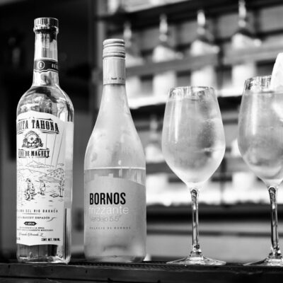 Elegant black and white image of cocktails and spirit bottles on a bar.