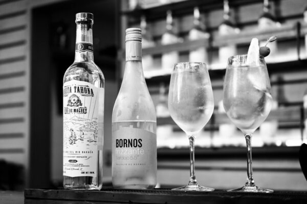 Elegant black and white image of cocktails and spirit bottles on a bar.