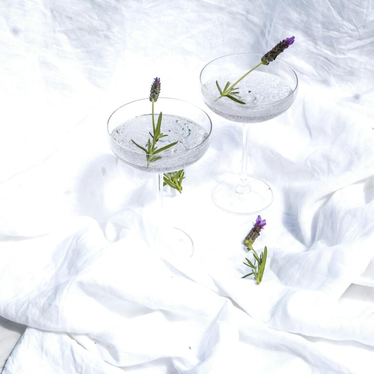 Two cocktail glasses with lavender, set on a white cloth background, creating a fresh and elegant scene.